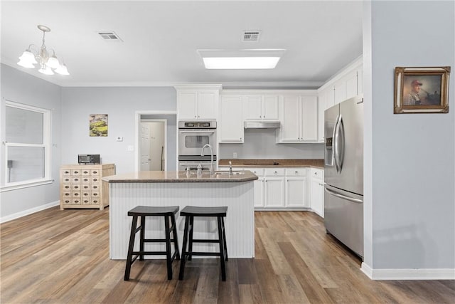 kitchen with crown molding, white cabinetry, hanging light fixtures, stainless steel appliances, and a center island with sink