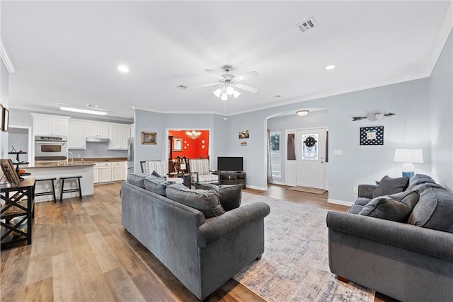 living room with crown molding, light hardwood / wood-style floors, and ceiling fan with notable chandelier