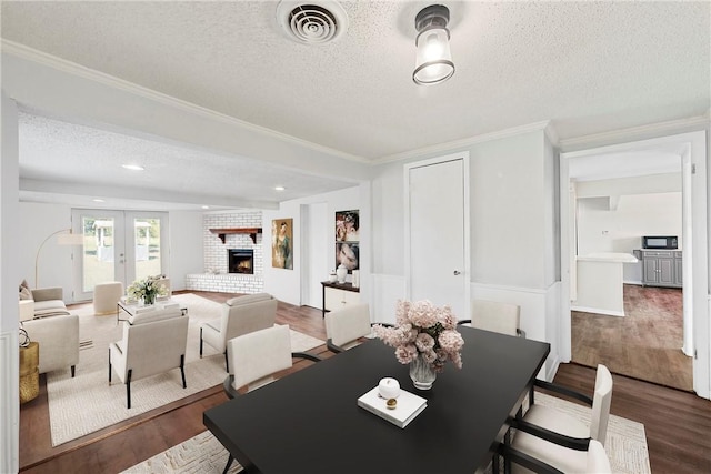 dining area featuring french doors, a brick fireplace, a textured ceiling, crown molding, and wood-type flooring