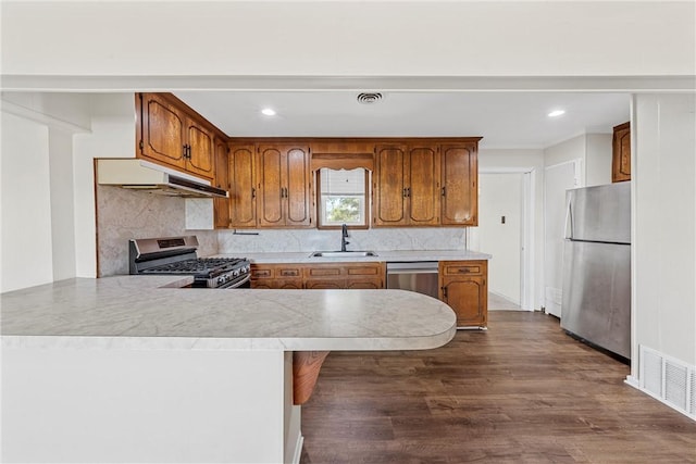 kitchen with kitchen peninsula, appliances with stainless steel finishes, tasteful backsplash, sink, and hardwood / wood-style flooring