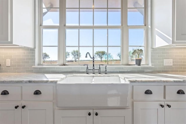 kitchen featuring decorative backsplash, white cabinetry, sink, and light stone countertops