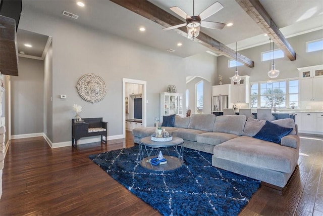 living room featuring a towering ceiling, ceiling fan, dark hardwood / wood-style flooring, and beamed ceiling