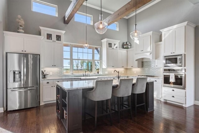 kitchen with white cabinetry, a kitchen island with sink, beamed ceiling, and appliances with stainless steel finishes