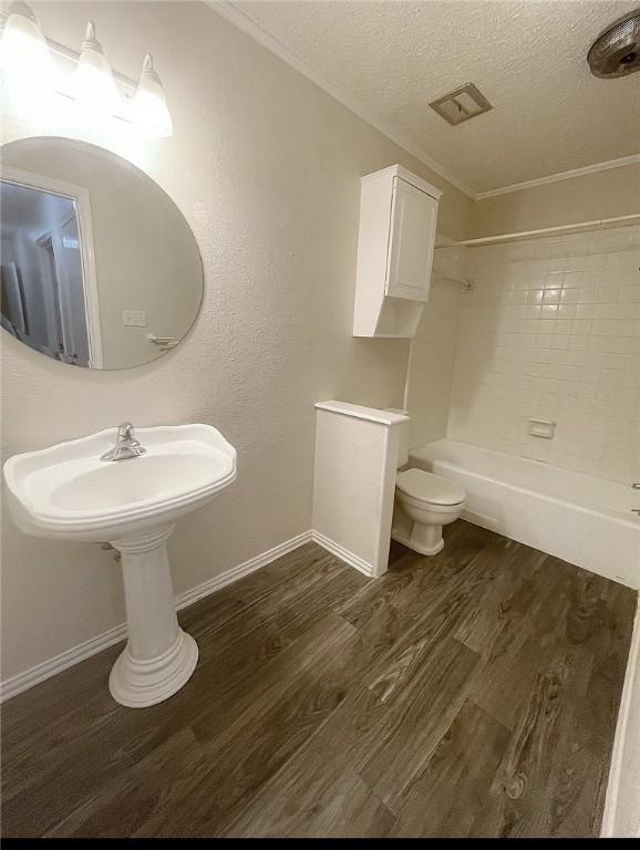 bathroom featuring tiled shower / bath, hardwood / wood-style flooring, toilet, ornamental molding, and a textured ceiling