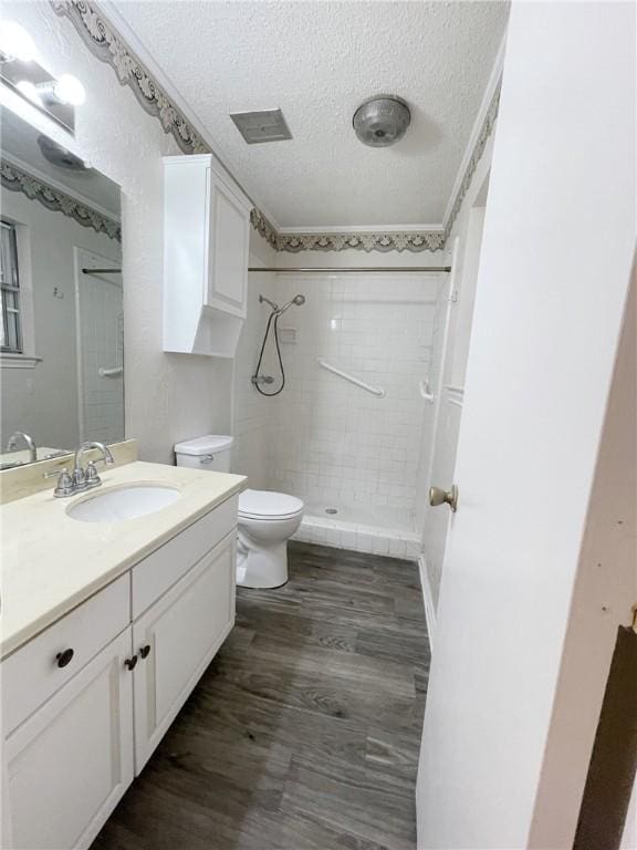 bathroom with vanity, toilet, a textured ceiling, tiled shower, and wood-type flooring