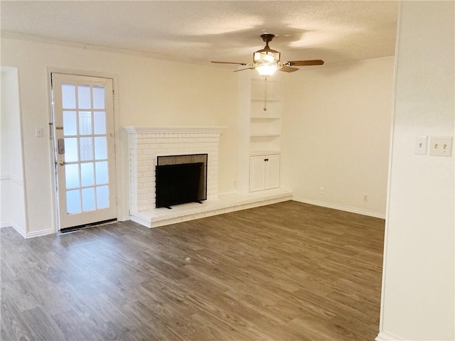 unfurnished living room with ceiling fan, dark wood-type flooring, a brick fireplace, a textured ceiling, and ornamental molding