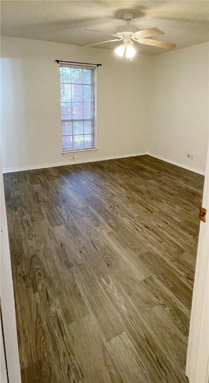 empty room with ceiling fan, dark wood-type flooring, and a textured ceiling