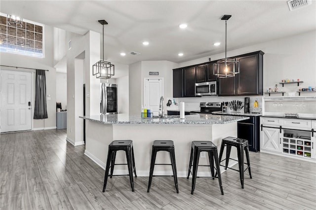 kitchen with light stone counters, appliances with stainless steel finishes, a kitchen bar, and a center island with sink