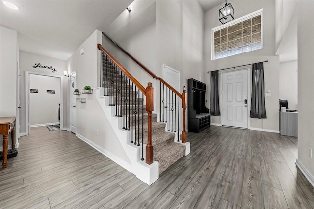 foyer with stairs, wood finished floors, a towering ceiling, and baseboards