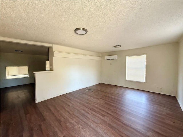 unfurnished room featuring an AC wall unit, dark wood-type flooring, and a textured ceiling