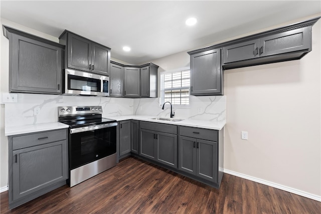 kitchen with sink, dark hardwood / wood-style flooring, backsplash, stainless steel appliances, and light stone counters