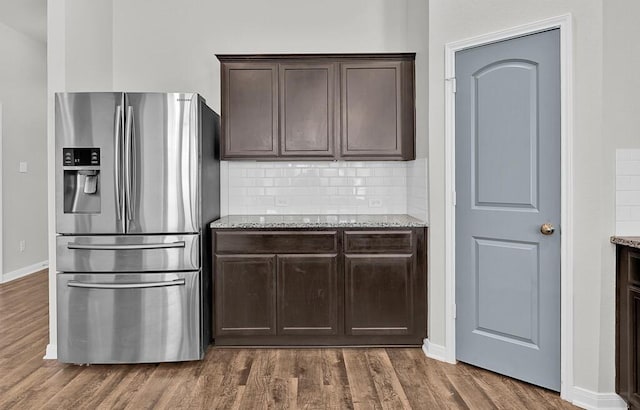 kitchen featuring light stone counters, dark hardwood / wood-style floors, stainless steel fridge, decorative backsplash, and dark brown cabinets