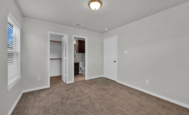 unfurnished bedroom featuring carpet flooring, a walk in closet, ensuite bathroom, and a closet