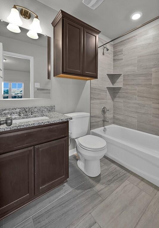 full bathroom featuring vanity, tiled shower / bath combo, and toilet