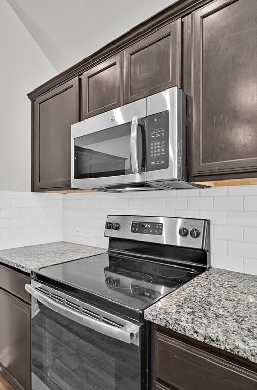 kitchen featuring tasteful backsplash, light stone counters, dark brown cabinets, and appliances with stainless steel finishes