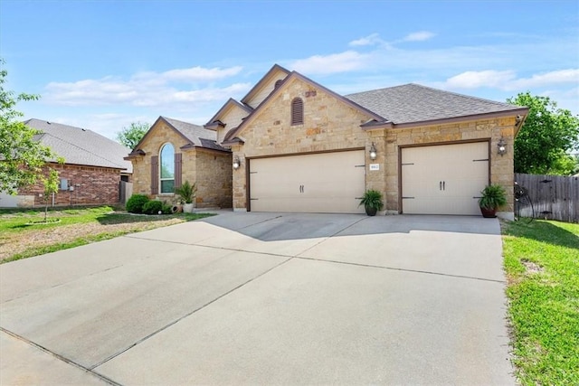 view of front of property featuring a garage, a shingled roof, fence, concrete driveway, and stone siding