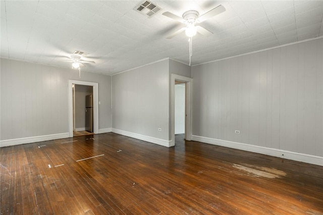 empty room featuring ceiling fan, crown molding, dark wood-type flooring, and wooden walls