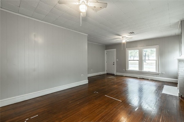 spare room with ceiling fan, wooden walls, dark hardwood / wood-style floors, and a brick fireplace