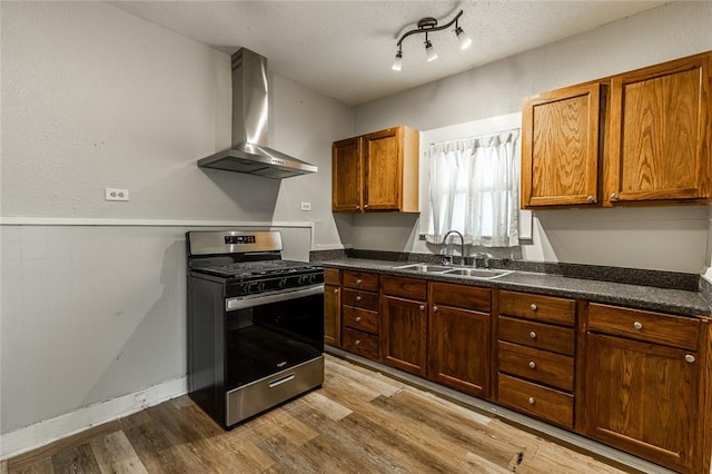 kitchen featuring wall chimney range hood, sink, gas range, light wood-type flooring, and a textured ceiling