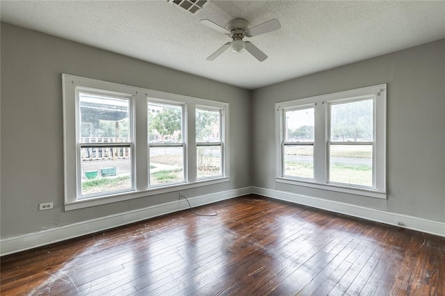 empty room with a textured ceiling, ceiling fan, a healthy amount of sunlight, and dark wood-type flooring