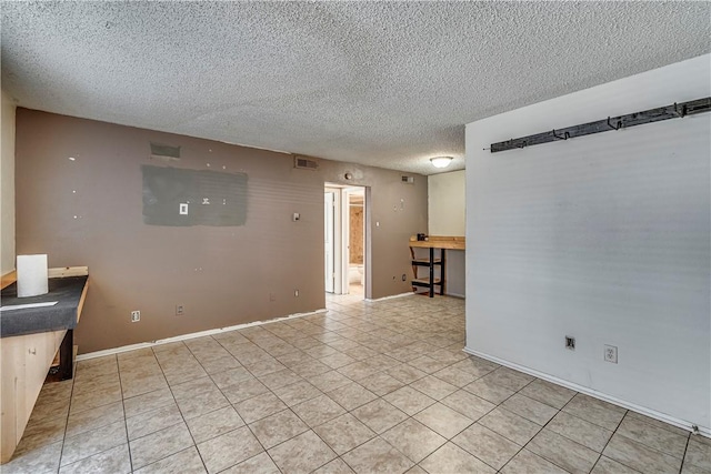 empty room with baseboards, visible vents, a textured ceiling, and light tile patterned flooring