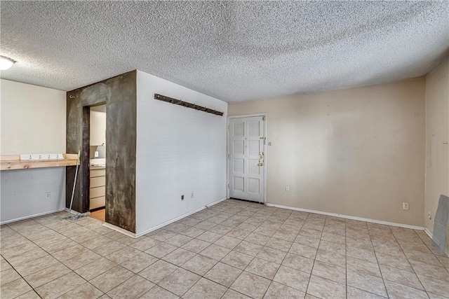 unfurnished room with a textured ceiling, light tile patterned flooring, and baseboards