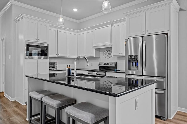 kitchen with sink, appliances with stainless steel finishes, dark stone counters, a kitchen island with sink, and white cabinets