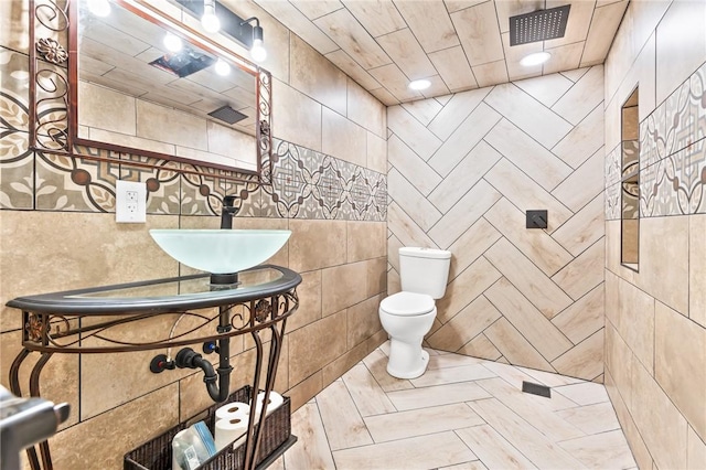 bathroom featuring walk in shower, sink, tile walls, and toilet