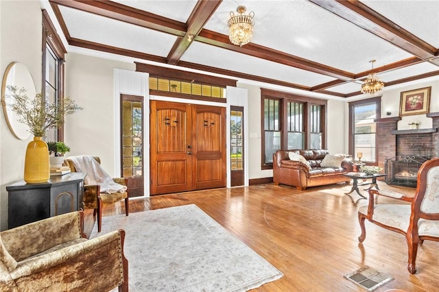 living room featuring coffered ceiling, a brick fireplace, an inviting chandelier, beamed ceiling, and wood-type flooring