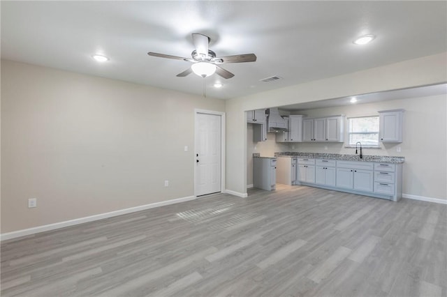 kitchen featuring sink, ceiling fan, light stone counters, light hardwood / wood-style floors, and wall chimney range hood