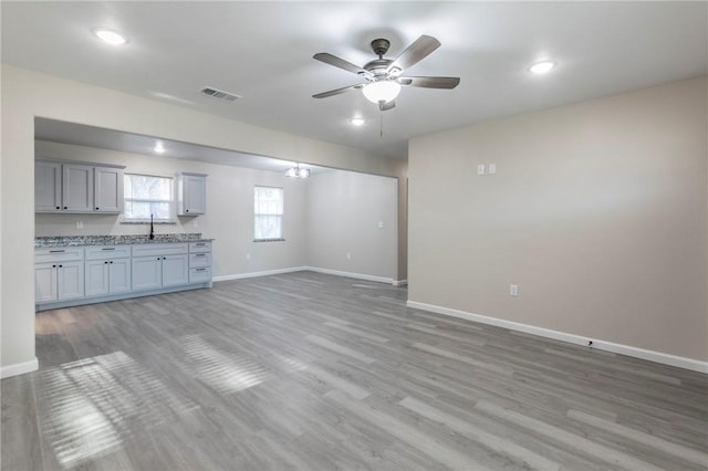 unfurnished living room featuring sink, ceiling fan with notable chandelier, and light hardwood / wood-style flooring