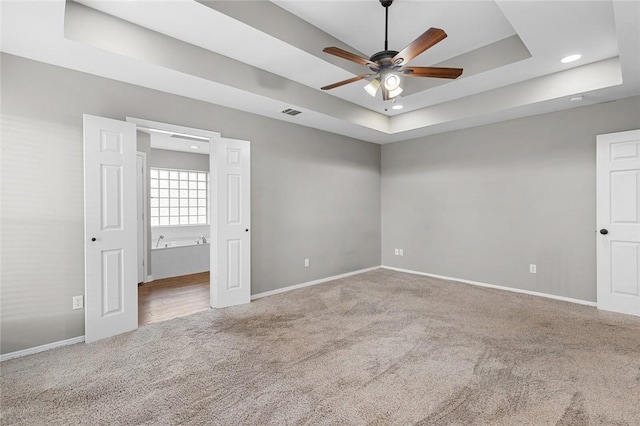 unfurnished bedroom with carpet flooring, a tray ceiling, ceiling fan, and ensuite bathroom