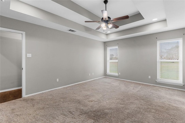 carpeted spare room featuring a raised ceiling and ceiling fan