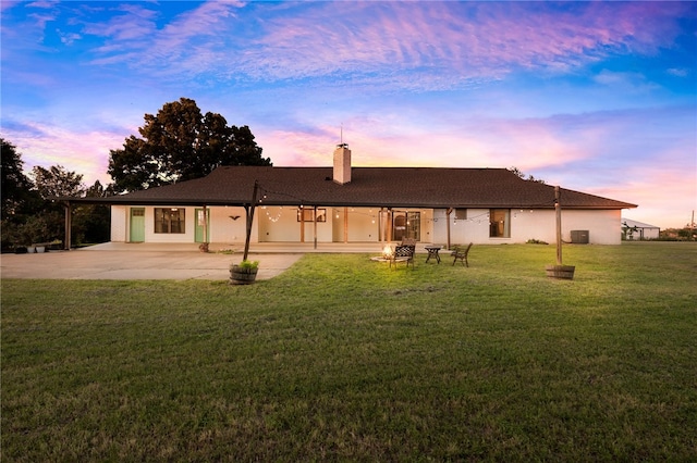 back house at dusk featuring a patio area and a lawn