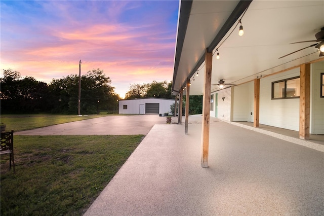 yard at dusk with ceiling fan, an outbuilding, and a garage