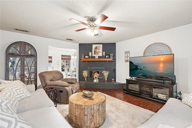 living room with a textured ceiling, ceiling fan, a fireplace, and dark hardwood / wood-style floors