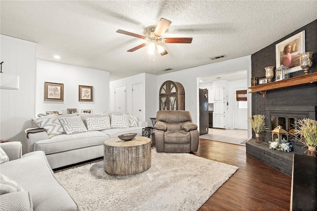 living room featuring a textured ceiling, ceiling fan, dark hardwood / wood-style flooring, and a fireplace