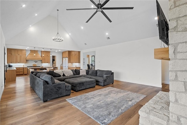 living room with ceiling fan with notable chandelier, light hardwood / wood-style floors, sink, and high vaulted ceiling