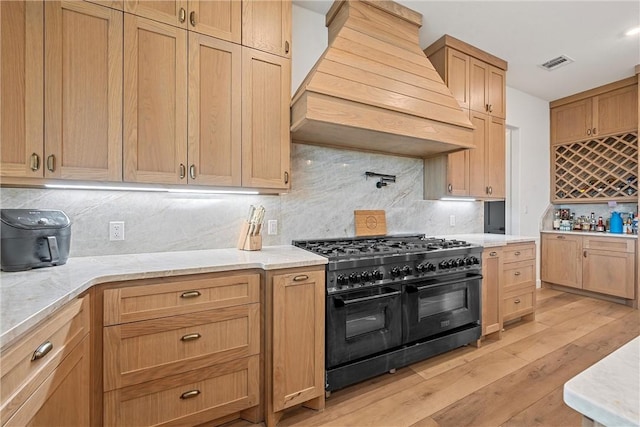 kitchen featuring backsplash, premium range hood, light stone counters, double oven range, and light hardwood / wood-style floors