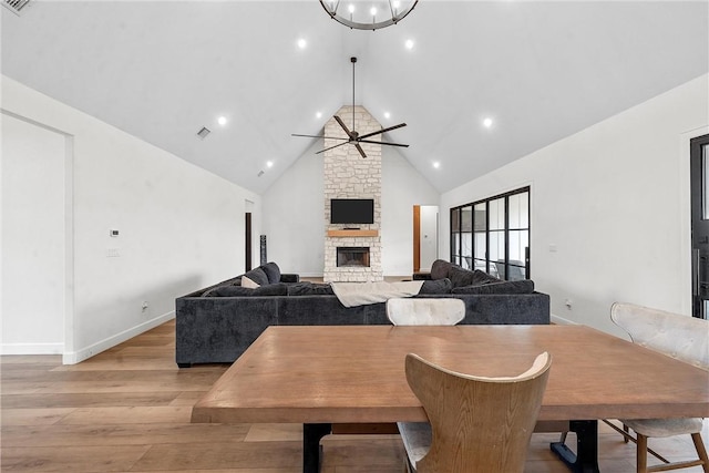 dining area featuring light wood-type flooring, high vaulted ceiling, a stone fireplace, and ceiling fan