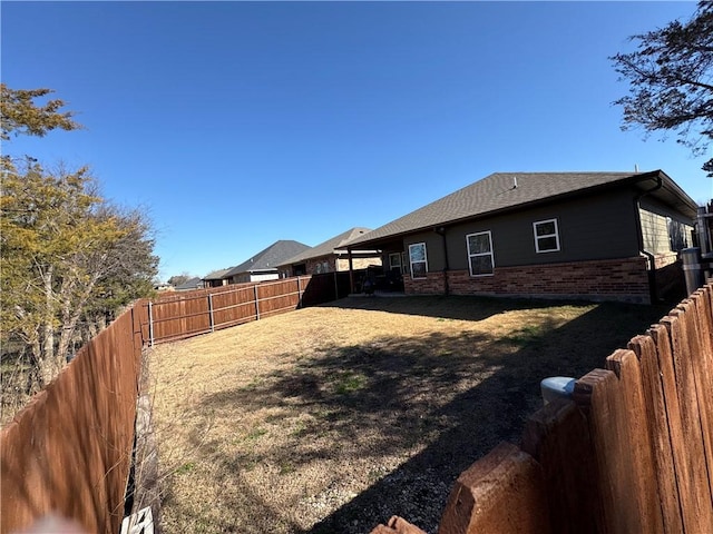 exterior space with a fenced backyard, a shingled roof, and brick siding