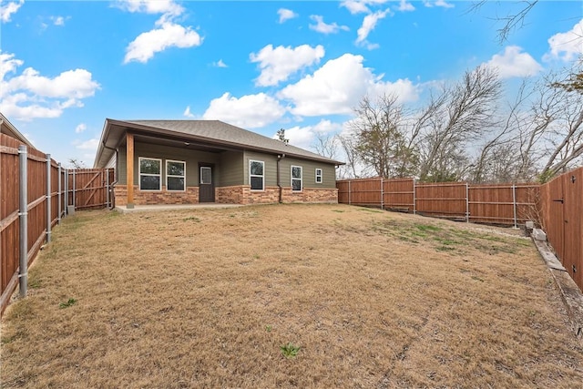 back of property featuring stone siding, a fenced backyard, and a yard