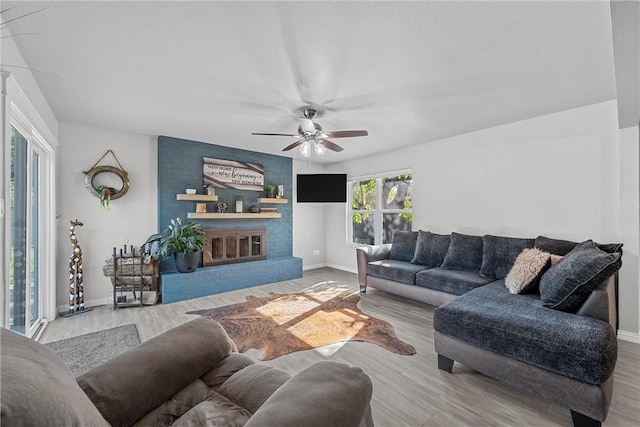 living room with light hardwood / wood-style floors, a brick fireplace, and ceiling fan