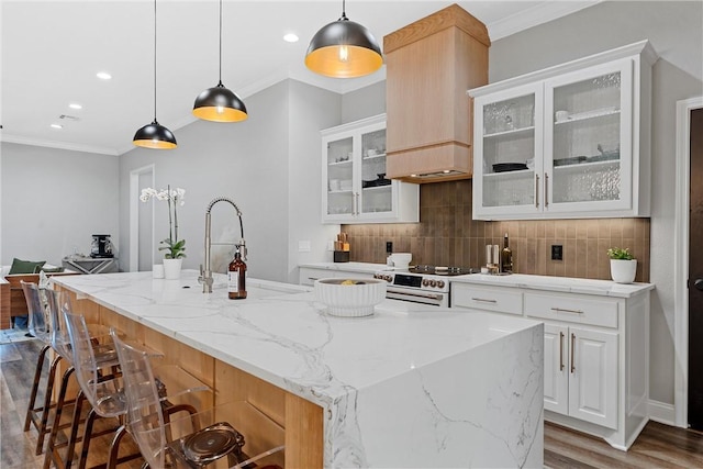 kitchen with decorative light fixtures, white range, white cabinetry, and an island with sink