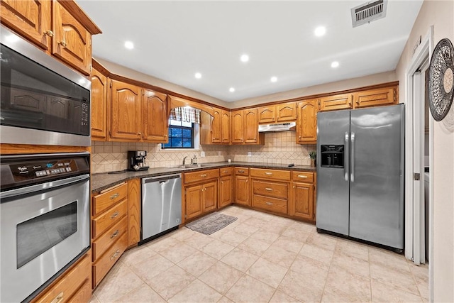 kitchen featuring appliances with stainless steel finishes, tasteful backsplash, dark stone counters, and sink