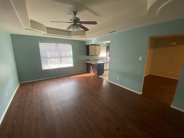 unfurnished living room featuring ceiling fan, dark wood-type flooring, and a tray ceiling