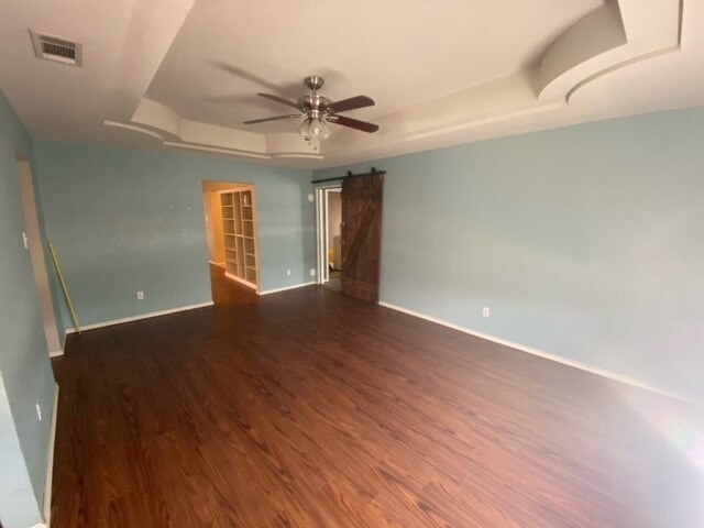 unfurnished room with a barn door, a tray ceiling, ceiling fan, and dark wood-type flooring