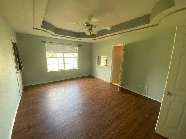 empty room with a raised ceiling, ceiling fan, and dark hardwood / wood-style floors