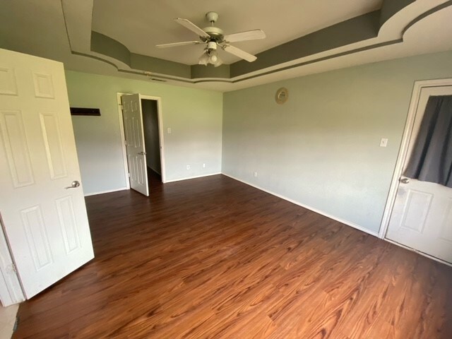 unfurnished room with dark hardwood / wood-style flooring, a raised ceiling, and ceiling fan