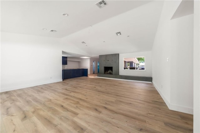 unfurnished living room with light wood-type flooring, a large fireplace, and vaulted ceiling